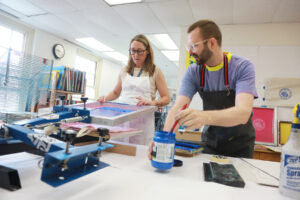 Courtney Quinn Hampton '00 silkscreens a Mary Washington College bag with Assistant Professor of Studio Art Coorain Devin as part of an Alumni College lecture. Photo by Karen Pearlman.