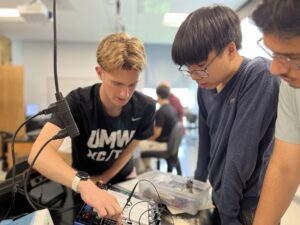 From left: CJ Hulleman '28, one of the PING program mentors, demonstrates to high schoolers Michael Young and Maiwand Barakzai how to construct a circuit that measures the effect of resonance, a physics concept that can be applied to engineering, biomedicine, and technology. Photo by Katie Van Houten '27.