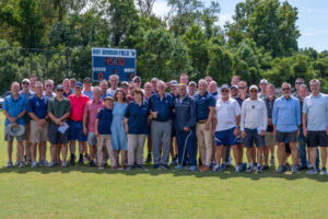 Coach Roy Gordon poses in front of the scoreboard that bears his name, along with his family, friends, former colleagues, UMW Athletics staff, and soccer alumni who contributed funding toward field renovations and facilities upgrades on the championship soccer field. Photo by Kaitlynn Kimball.