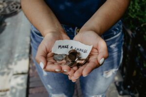Cupped hands holding a small slip of paper that says "Make a Change" and a handful of coins. 