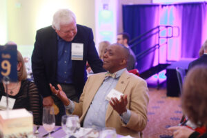 Chief of Staff Emeritus Marty Wilder '80 (left) stands and talks to Associate Vice President and Dean of Student Life Emeritus Cedric Rucker '81, who is seated and gesturing with his hands.