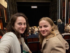 Description: Two college students turning to look at the camera at the Opéra Bastille in Paris. Caption: Carly (right) Brianna Kenealy '25 (left) a production of 'I puritani' at the Opéra Bastille during their study abroad in Paris. Photo courtesy of Carly Radgowski.