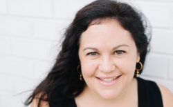 2001 alumna Jessica McCaughey smiling against a white brick background.