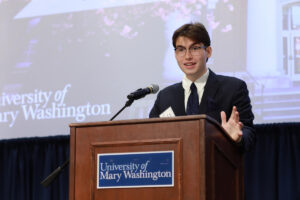 A student at a podium with a University of Mary Washington sign.