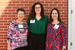 Two donors and a student recipient standing in front of a brick wall.