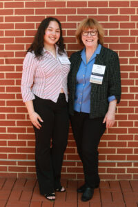 A smiling student and alumni donor in front of a brick wall.