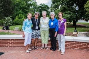 A group of five 1966 alumnae standing outside in front of a low brick wall.