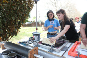 A student demonstrates how to screen-print a shirt to another student.
