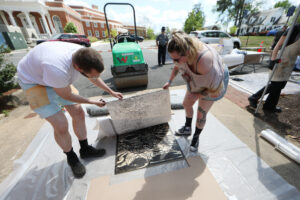 A professor and student check the student's print with the rented steamroller in the background.
