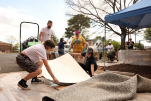 Two students place paper for another student's print while that student and the professor watch. The steamroller is in the background.