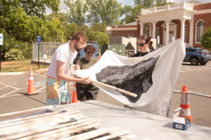 A professor and two students hang a finished print on cloth up to dry.