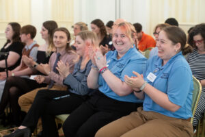 A row of students clap, including two Washington Guides in blue branded shirts.