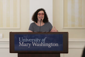 A professor speaks at a podium with a sign that reads University of Mary Washington.