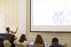 A student standing at a podium points up at a screen.
