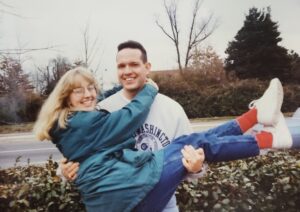 An early '90s photo of a couple; the husband is holding the wife in his arms and her arms are around his neck.