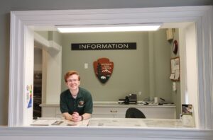 A smiling student in front of a National Park Service plaque with a large sign that says 'Information.'