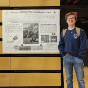 A student smiling and standing next to his poster.