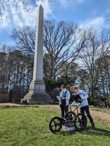 A student and professor using ground-penetrating radar in front of the Mary Washington monument.