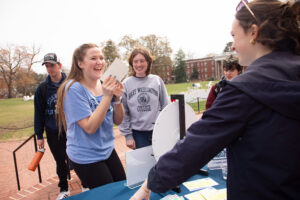 A student spins a wheel while interacting with a volunteer while two others look on.