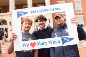Three students in front of the Cedric Rucker University Center holding up a frame that reads #MaryWashDay and We love Mary Wash.