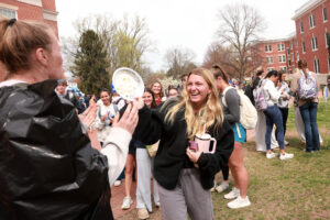 A student pies a volunteer in the face while onlookers have fun in the background.