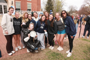 A group of UMW women's lacrosse players holding a pie. One is wearing a plastic bag and has just been pied in the face.