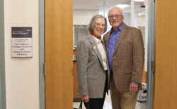 A couple standing in the doorway of a laboratory with their names on the plaque.