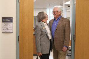 A couple standing in the doorway of a laboratory with their names on the plaque.