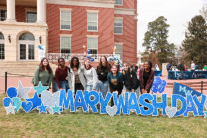 A group of students standing behind the Mary Wash Day sign in front of the Cedric Rucker University Center.