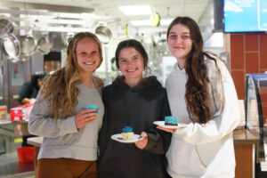 Three students in the UMW Dining facility holding blue desserts.