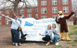 Students with the Spirit Rock that has information about Mary Wash Day. UMW mascot Sammy D. Eagle stands on the right.
