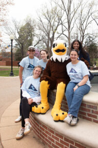 Students sitting on the UMW fountain in front of Monroe Hall, surrounding UMW mascot Sammy D. Eagle.