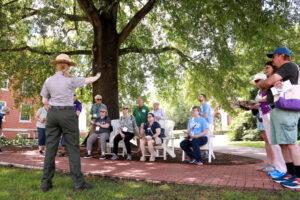 A group of alumni and guests seated under a tree listening to a National Park Ranger.
