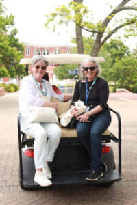Two alumnae seated on the back of a golf cart.