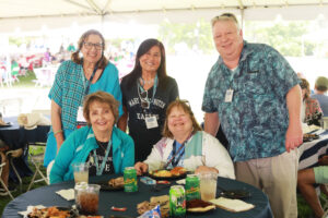 A group of 1979 alumni and guests under a tent and seated at a table during the Ball Circle picnic during Reunion Weekend.