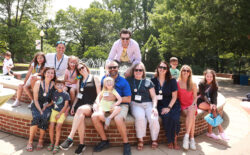 Alumni with their kids, several of whom have painted faces, seated at the fountain in front of Monroe Hall during Reunion Weekend.