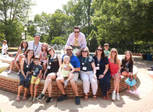 Alumni with their kids, several of whom have painted faces, seated at the fountain in front of Monroe Hall during Reunion Weekend.