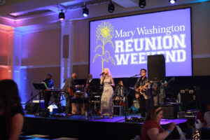 A live band performing with a Mary Washington Reunion Weekend screen behind them.