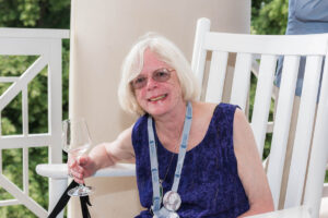 An alumna seated in a rocking chair with a glass of wine. 