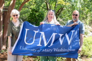 Three alumni holding a UMW flag at the Jepson Alumni Executive Center.