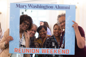 Five 1976 alumnae pose for a photo with a photo frame that reads 'Mary Washington Alumni Reunion Weekend.'
