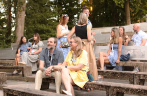A couple sit on the Heslep Amphitheatre steps during a 'Bites and Sites' event. Other alumni and students stand around in the background.