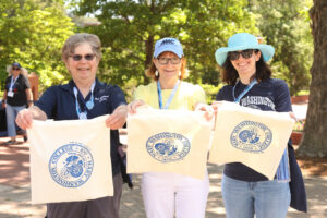 Three alumnae standing on Campus Walk hold out the bags they screenprinted with a Mary Washington College logo.