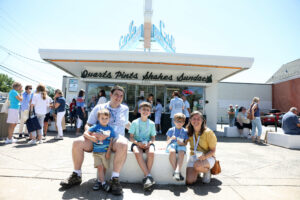 A family enjoys ice cream at Carl's. Other alumni eat and order ice cream in the background.