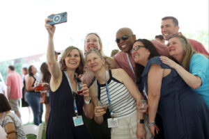 A group of 1990s alumni take a selfie while holding wine glasses.