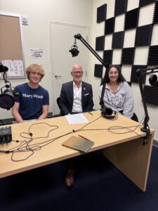 Two students and President Paino sitting in a podcast studio, smiling at the camera.