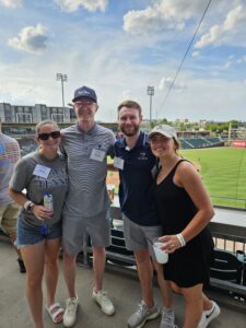 A group of four people wearing Mary Washington gear at a minor league baseball stadium.