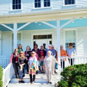 A group of people standing on the steps of a white house with railings and a haint blue porch ceiling.