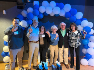 A group of six people standing under a blue and gray balloon arch.