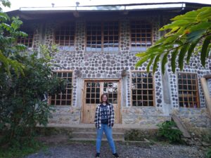 A UMW student in front of a stone building in Guatemala, with tropical trees off to the side.